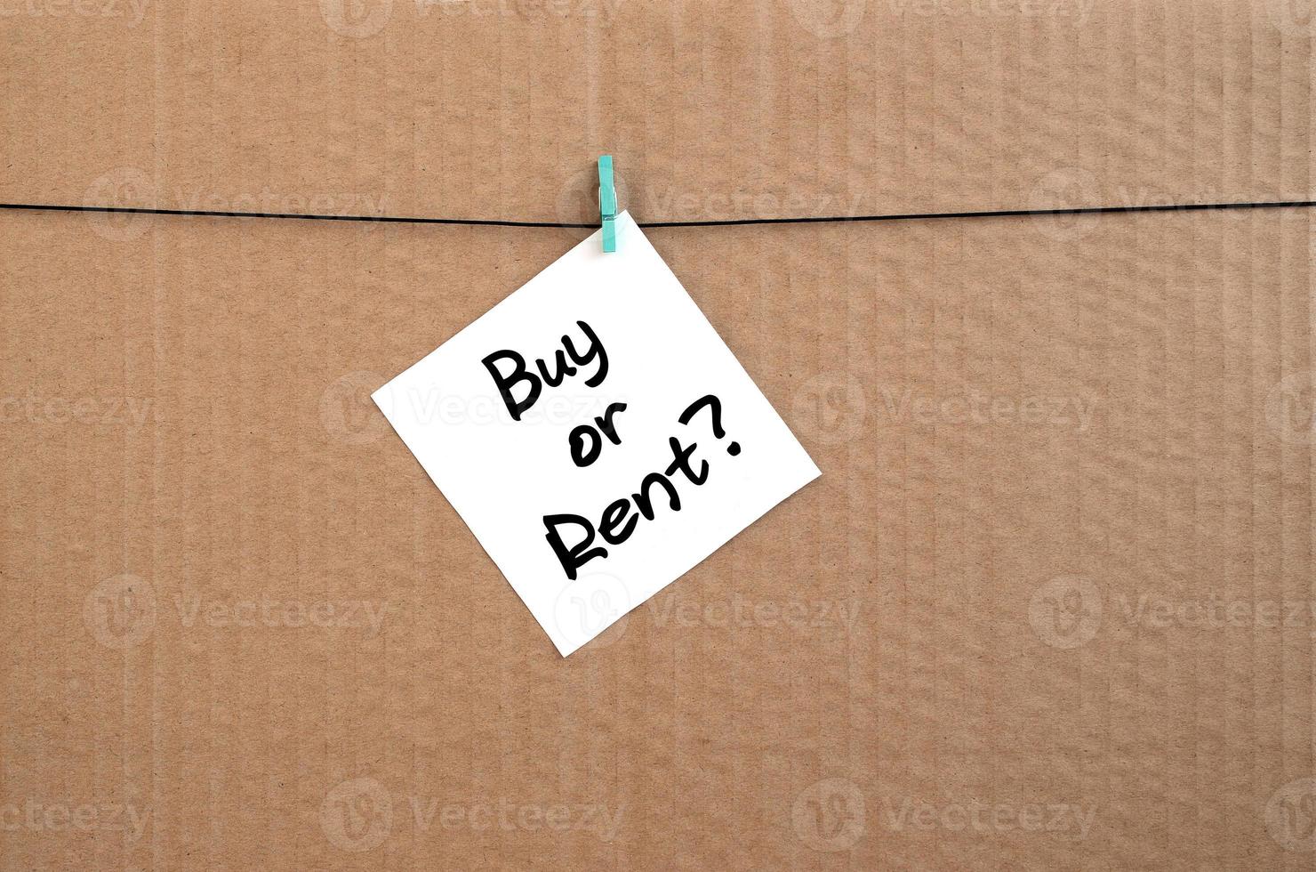 Buy or rent Note is written on a white sticker that hangs with a clothespin on a rope on a background of brown cardboard photo