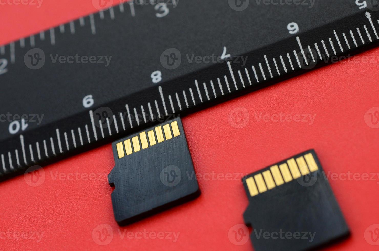 Two small micro SD memory cards lie on a red background next to a black ruler. A small and compact data and information store photo