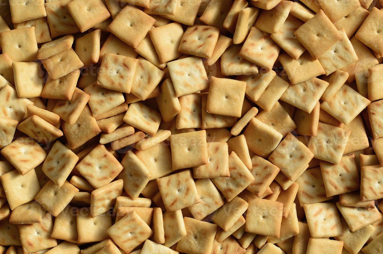 A lot of small cookies are square shaped. A pattern of a yellow salt cracker. Background image with salted pastry photo