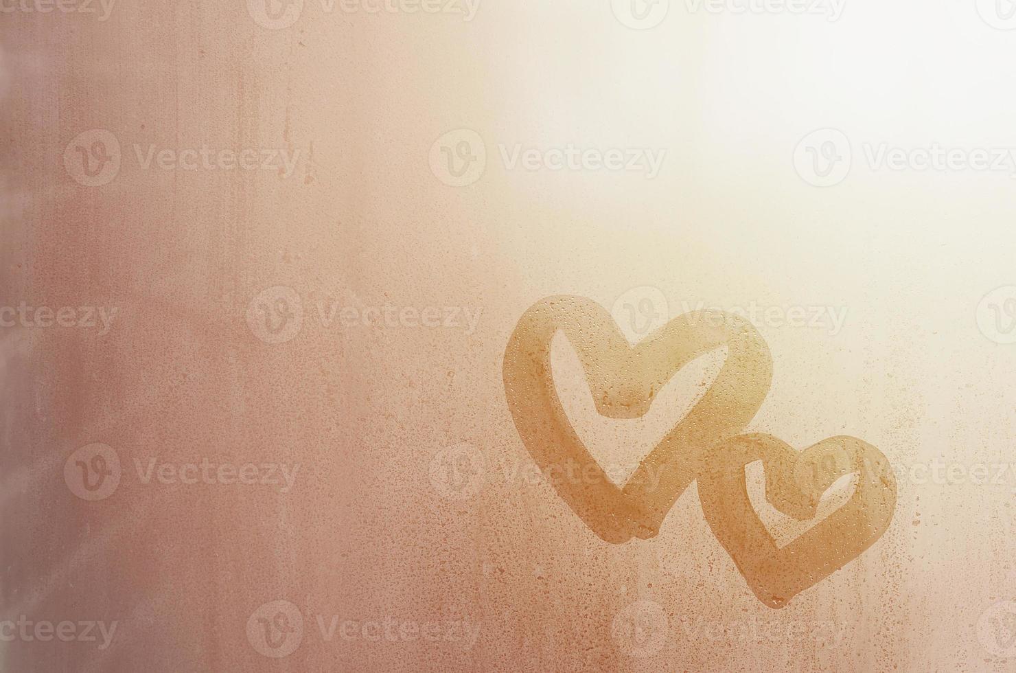 Couple of abstract blurred love heart symbol drawn by hand on the wet window glass with sunlight background. Template for Valentine Day postcards photo