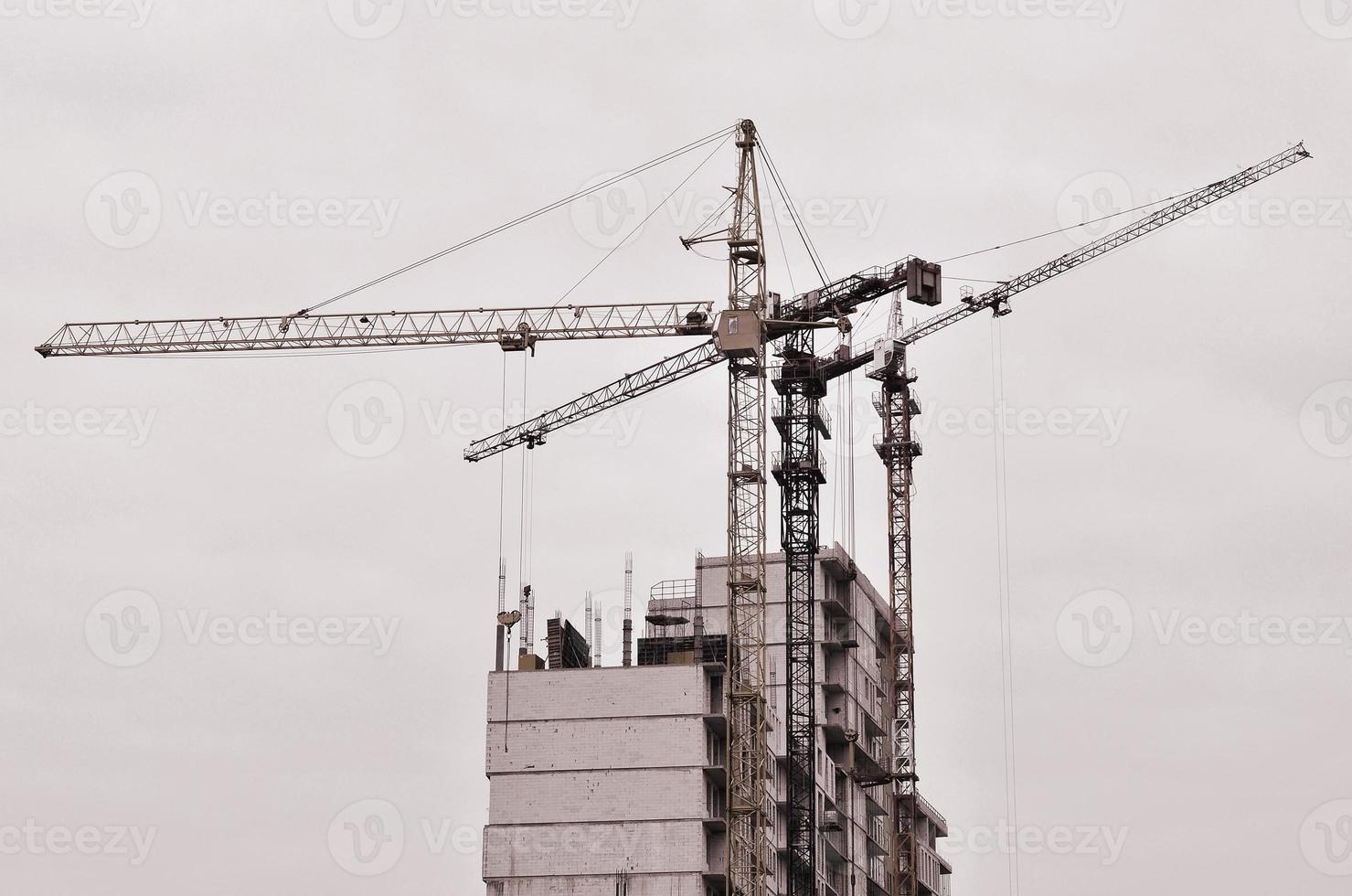 Working tall cranes inside place for with tall buildings under construction against a clear blue sky. Crane and building working progress. Retro tone photo