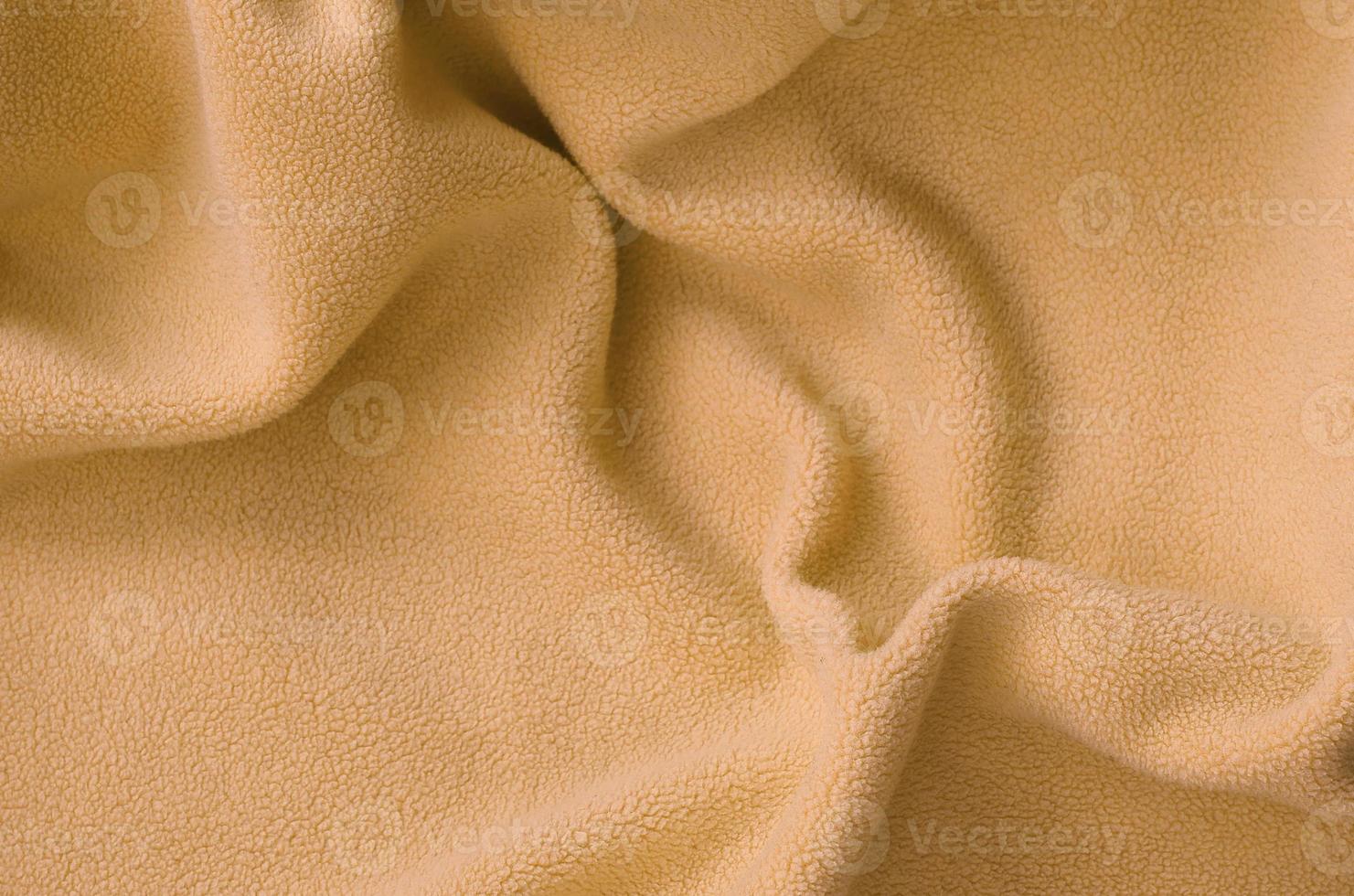 The blanket of furry orange fleece fabric. A background of light orange soft plush fleece material with a lot of relief folds photo