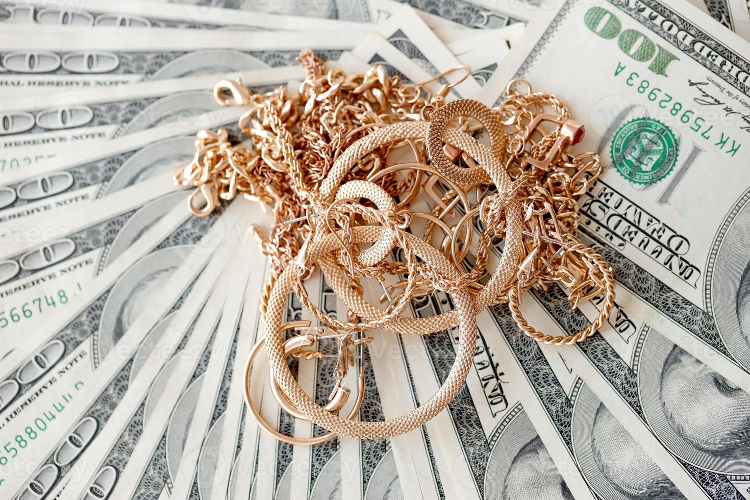 muchos costosos anillos de joyería de oro, aretes y collares en una gran cantidad de billetes de dólares estadounidenses de cerca. casa de empeño o joyería foto