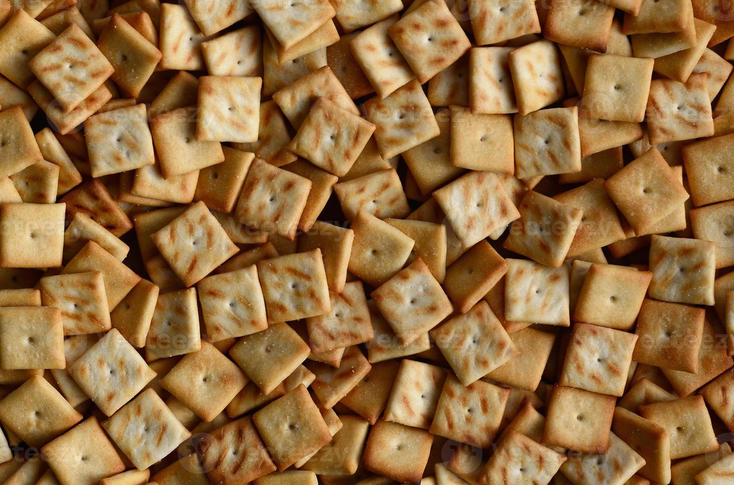 A lot of small cookies are square shaped. A pattern of a yellow salt cracker. Background image with salted pastry photo