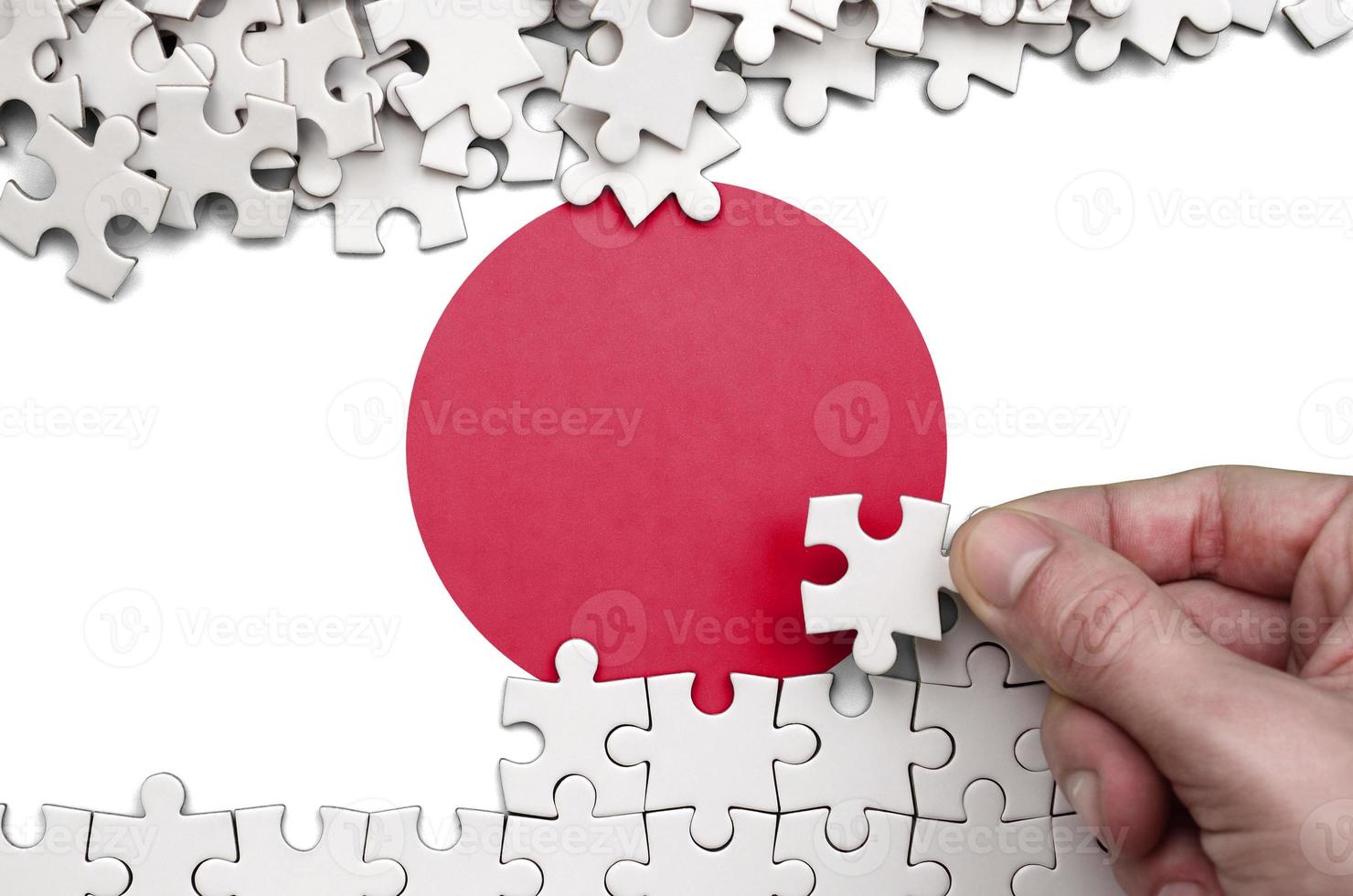 Japan flag  is depicted on a table on which the human hand folds a puzzle of white color photo