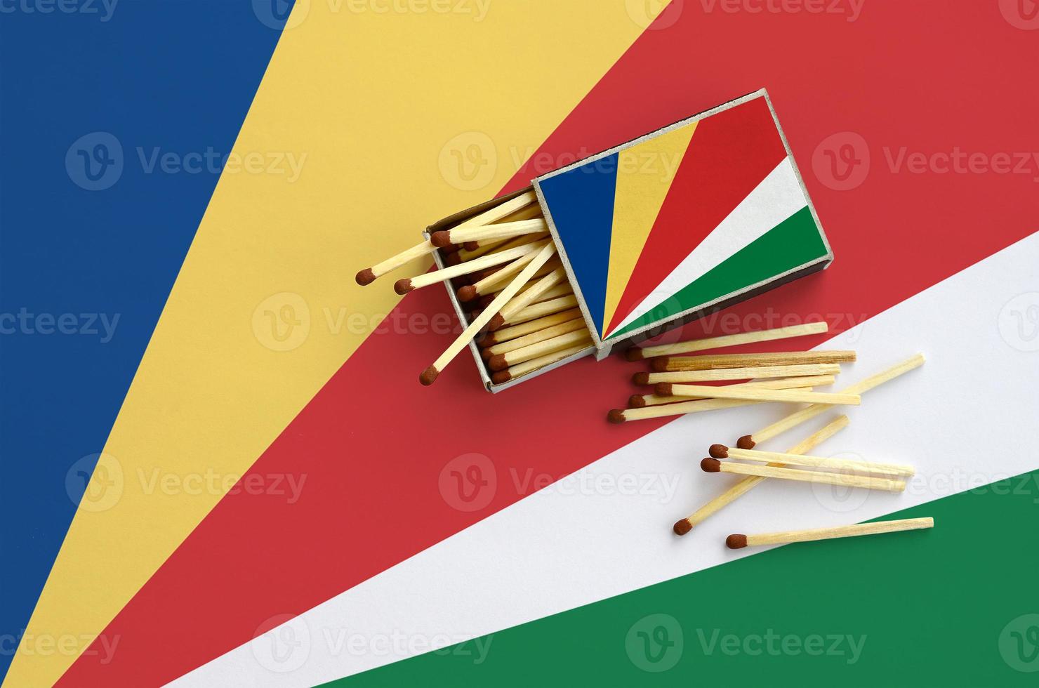 Seychelles flag  is shown on an open matchbox, from which several matches fall and lies on a large flag photo