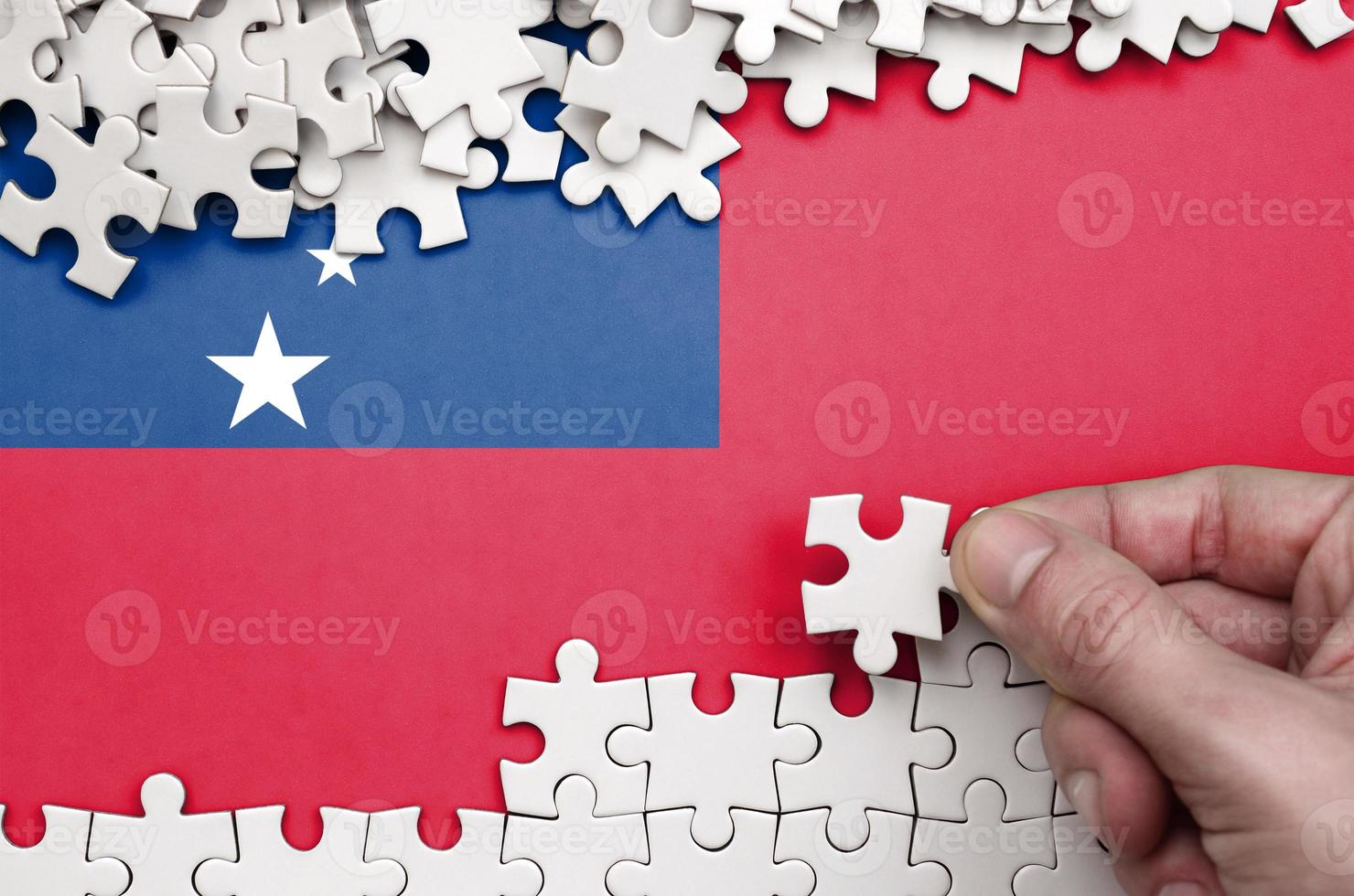 Samoa flag  is depicted on a table on which the human hand folds a puzzle of white color photo