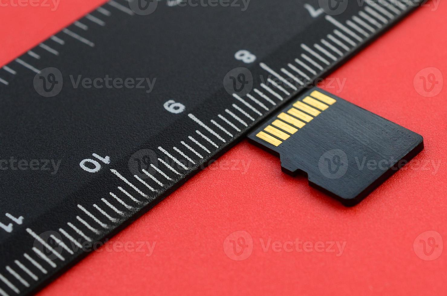 Small micro SD memory card lie on a red background next to a black ruler. A small and compact data and information store photo