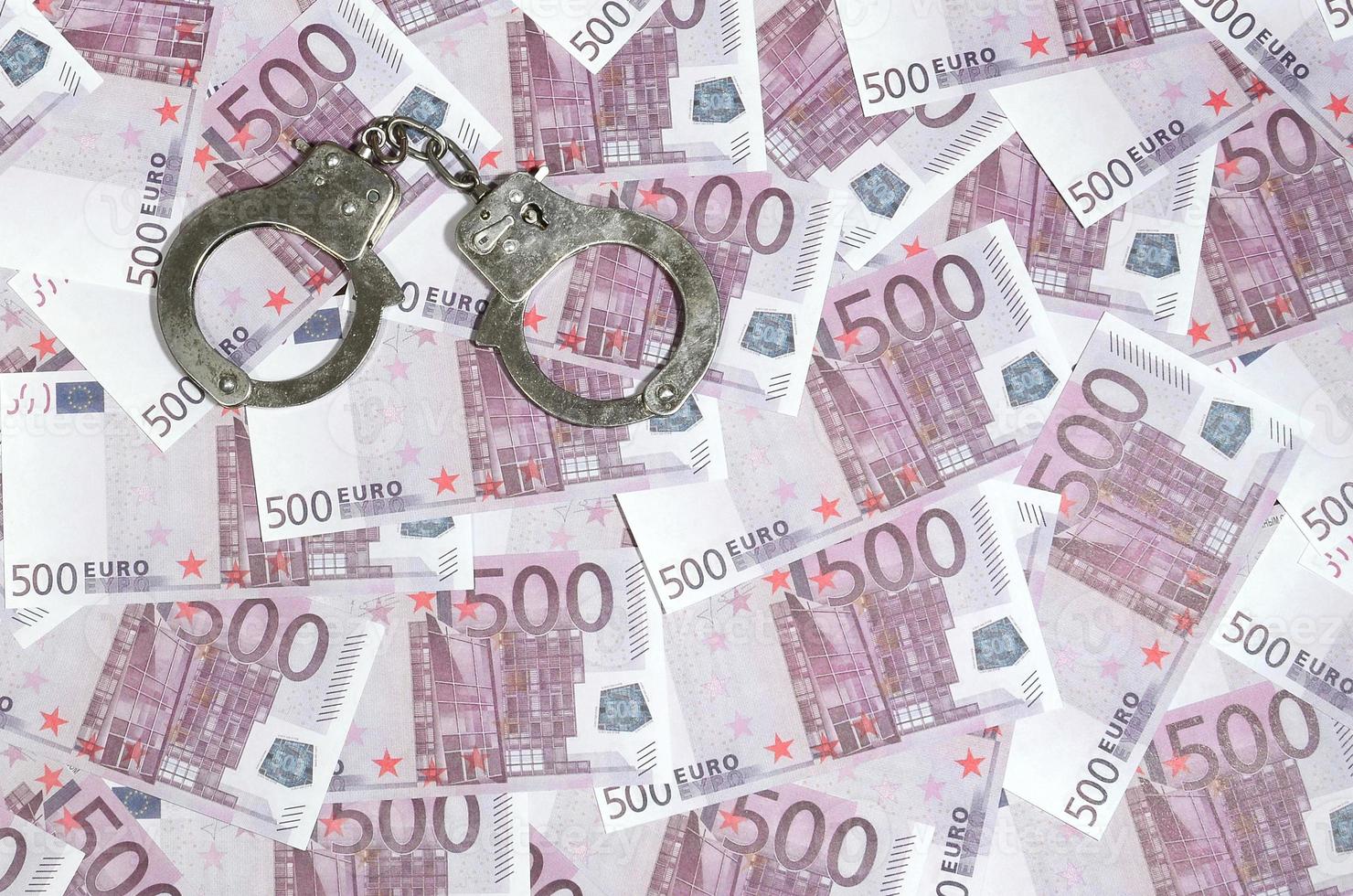 Handcuffs on five hundred euros background. Financial crime, dirty money and corruption concept - 500 money bills and dirty steel handcuffs photo