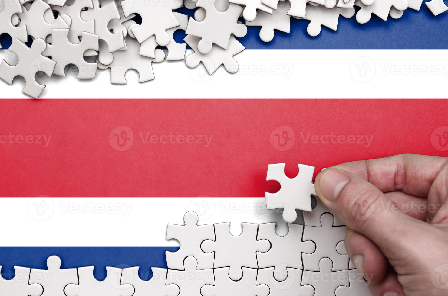 Costa Rica flag  is depicted on a table on which the human hand folds a puzzle of white color photo