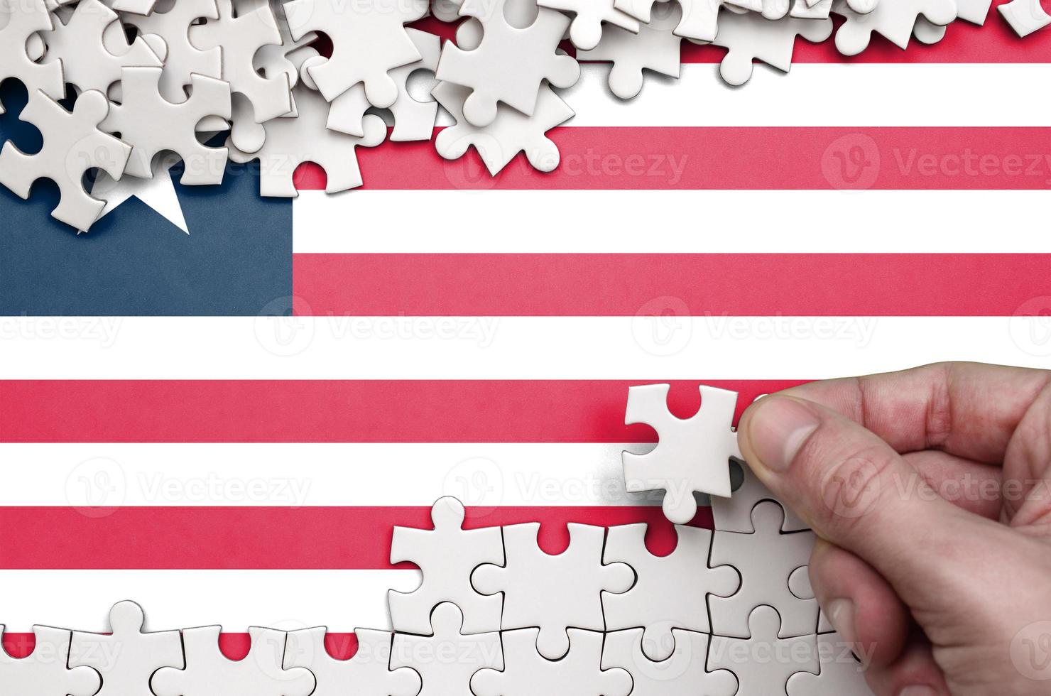 Liberia flag  is depicted on a table on which the human hand folds a puzzle of white color photo