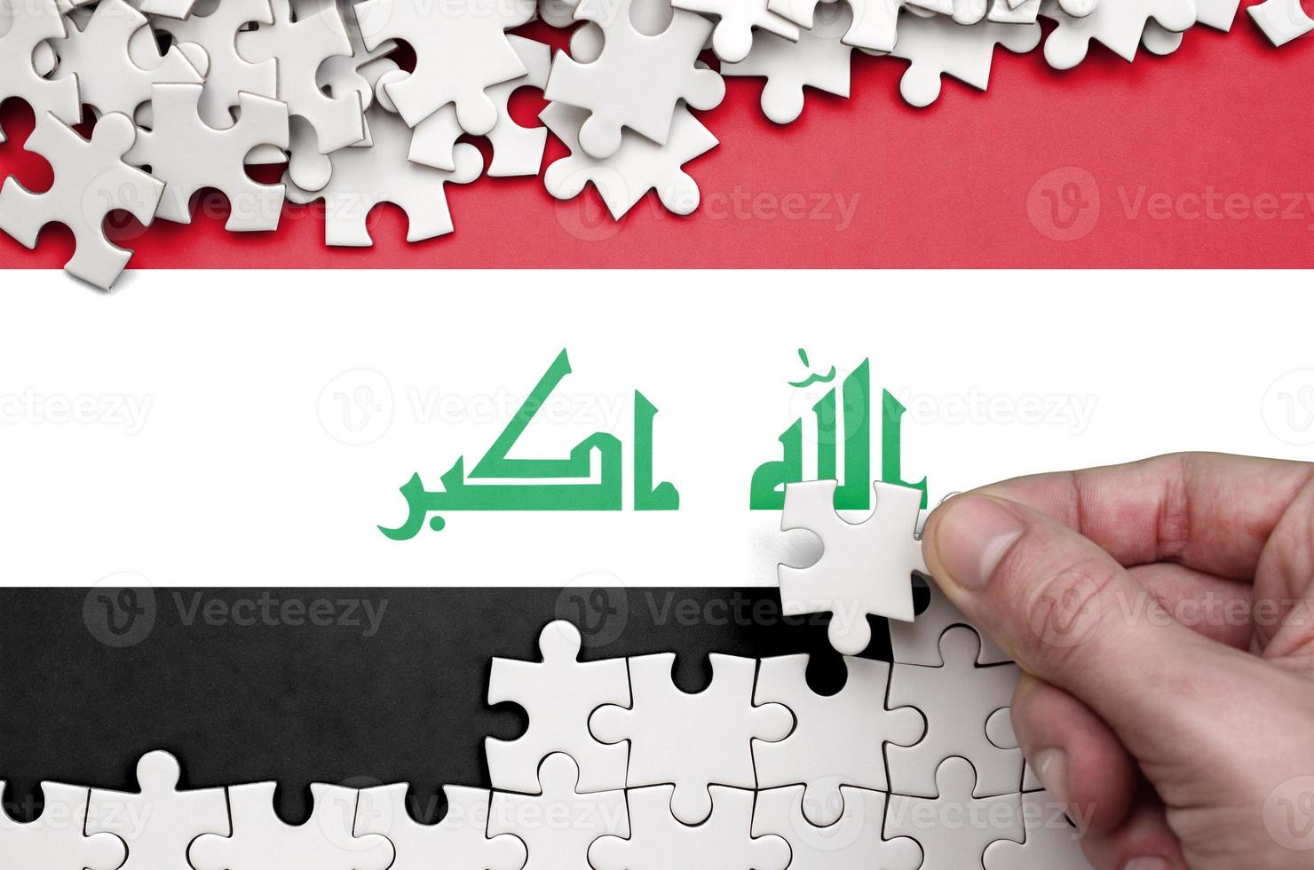 Iraq flag  is depicted on a table on which the human hand folds a puzzle of white color photo