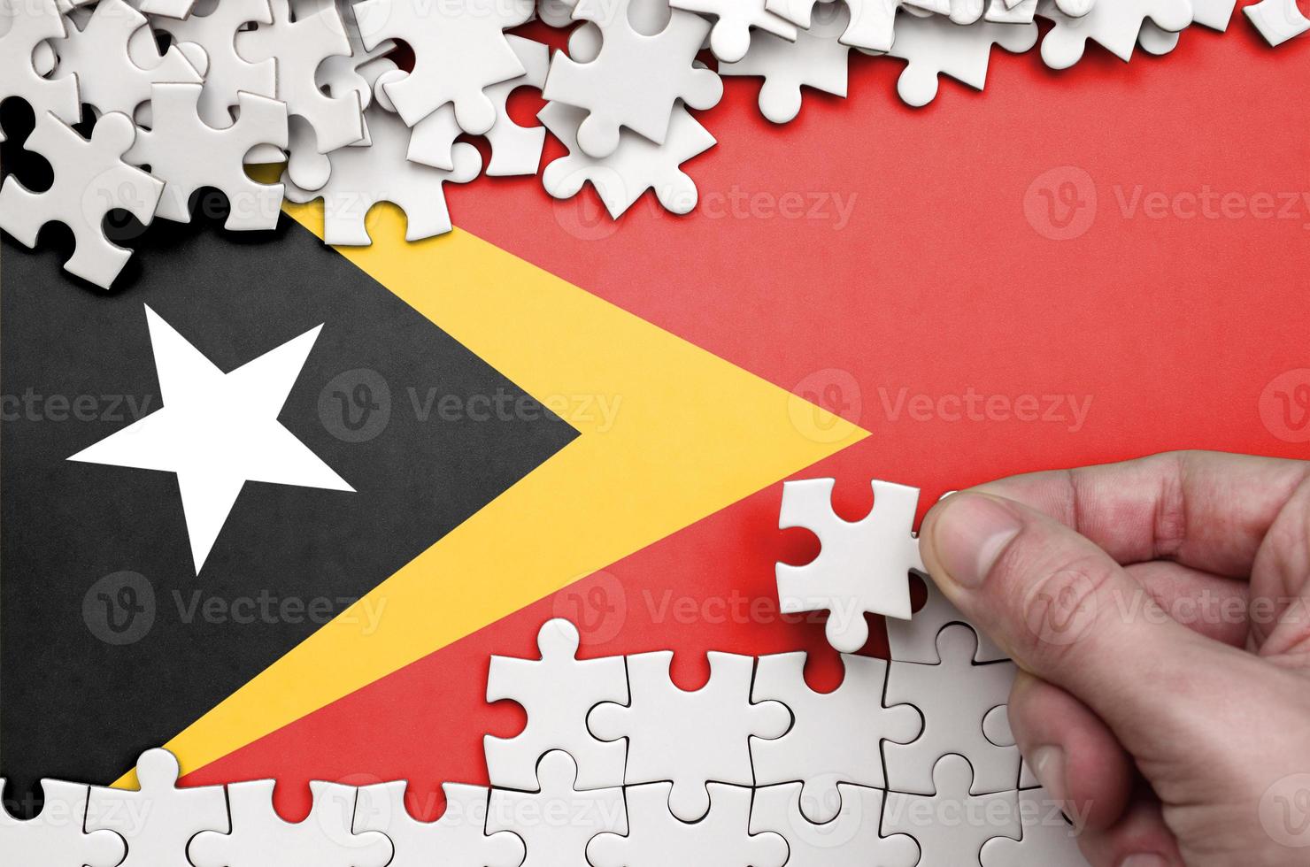 Timor Leste flag  is depicted on a table on which the human hand folds a puzzle of white color photo