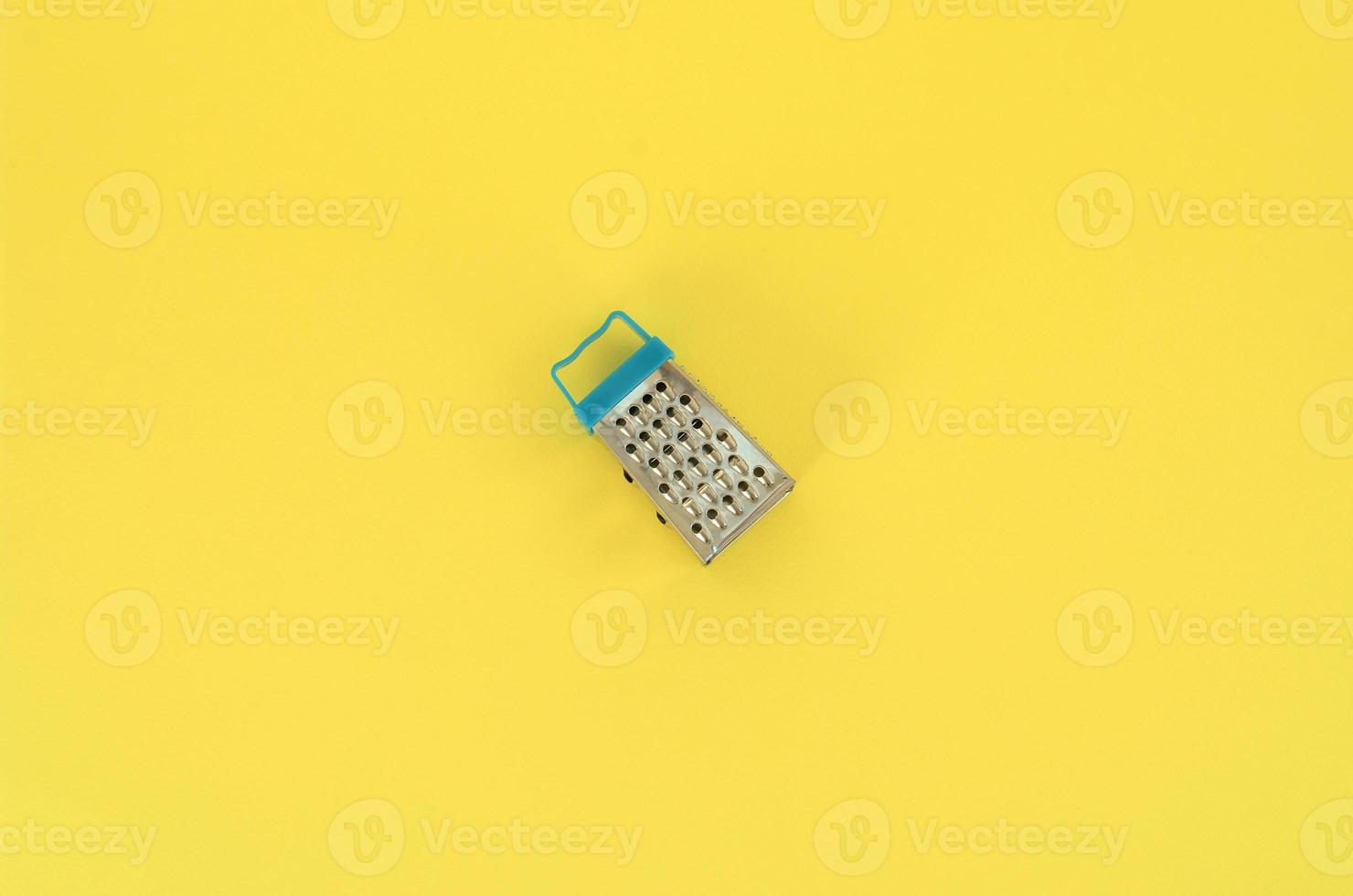 Stainless steel grater lies on a pastel colored paper. Kitchen accessories. Tools for cooking. Flat lay top view photo