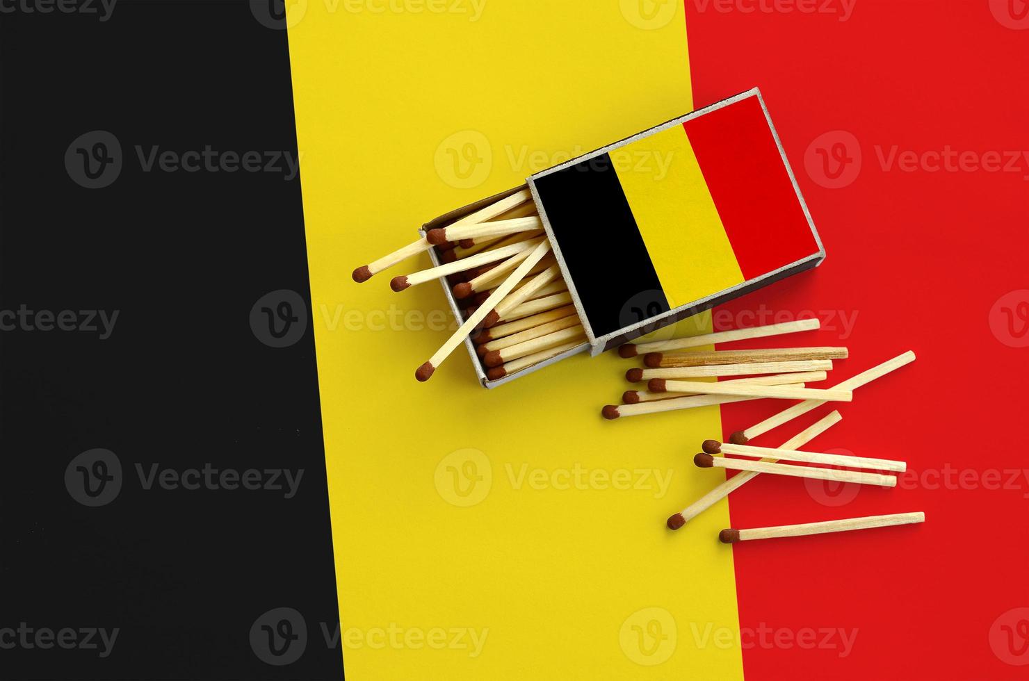 Belgium flag  is shown on an open matchbox, from which several matches fall and lies on a large flag photo