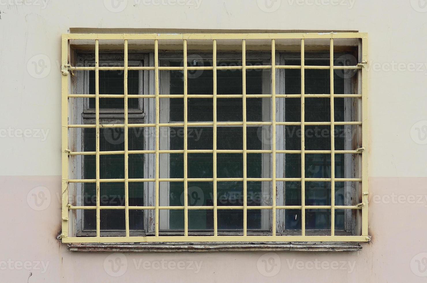 The texture of the wall of a residential building with a window that is protected by a metal grill. Old method of protecting housing from robbers photo