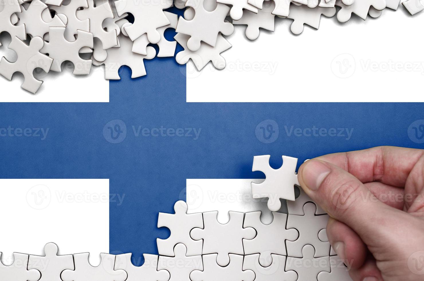 Finland flag  is depicted on a table on which the human hand folds a puzzle of white color photo