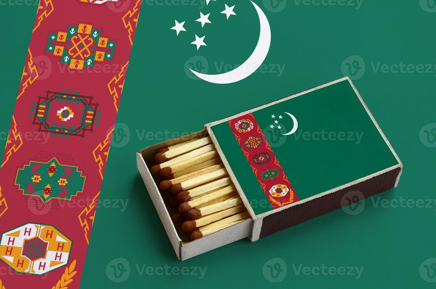 Turkmenistan flag  is shown in an open matchbox, which is filled with matches and lies on a large flag photo