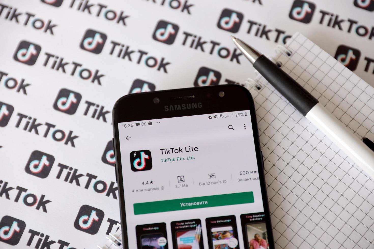 TERNOPIL, UKRAINE - MAY 2, 2022 Tik Tok smartphone app on screen and Many TikTok logo printed on paper. Tiktok or Douyin is a famous Chinese short-form video hosting service owned by ByteDance photo