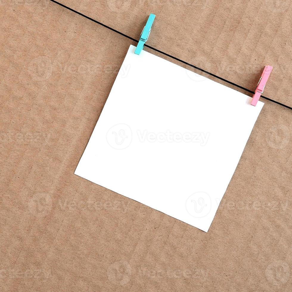 White blank card on rope on a brown cardboard background. Creative reminder, small sheet of paper on wooden clothespin, memo backdrop photo