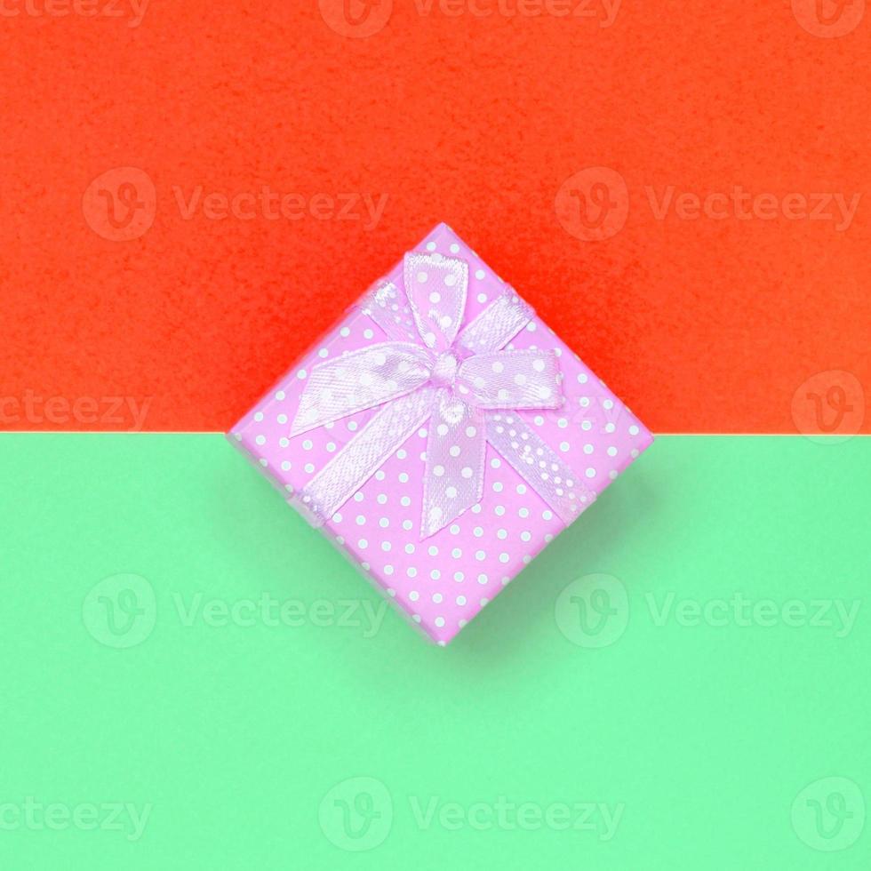 Small pink gift box lie on texture background of fashion pastel turquoise and red colors paper photo