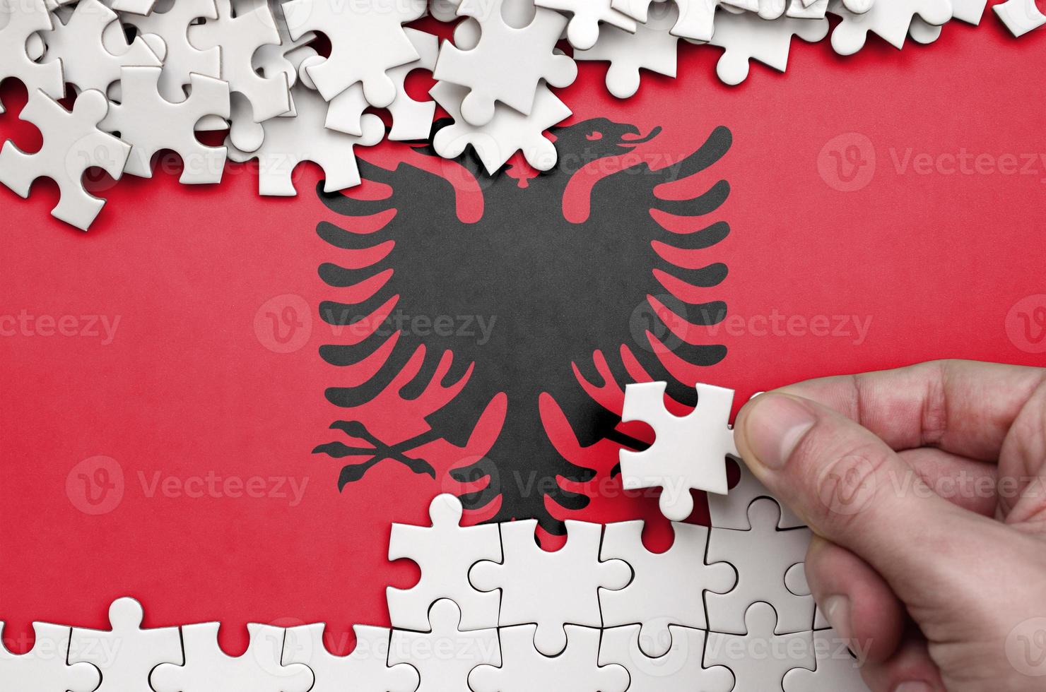 Albania flag  is depicted on a table on which the human hand folds a puzzle of white color photo