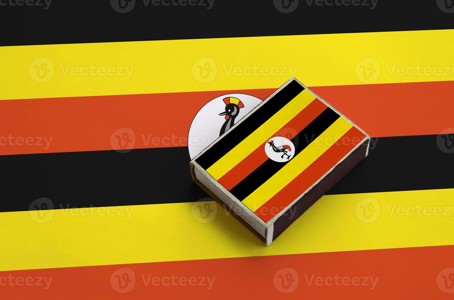 Uganda flag  is pictured on a matchbox that lies on a large flag photo