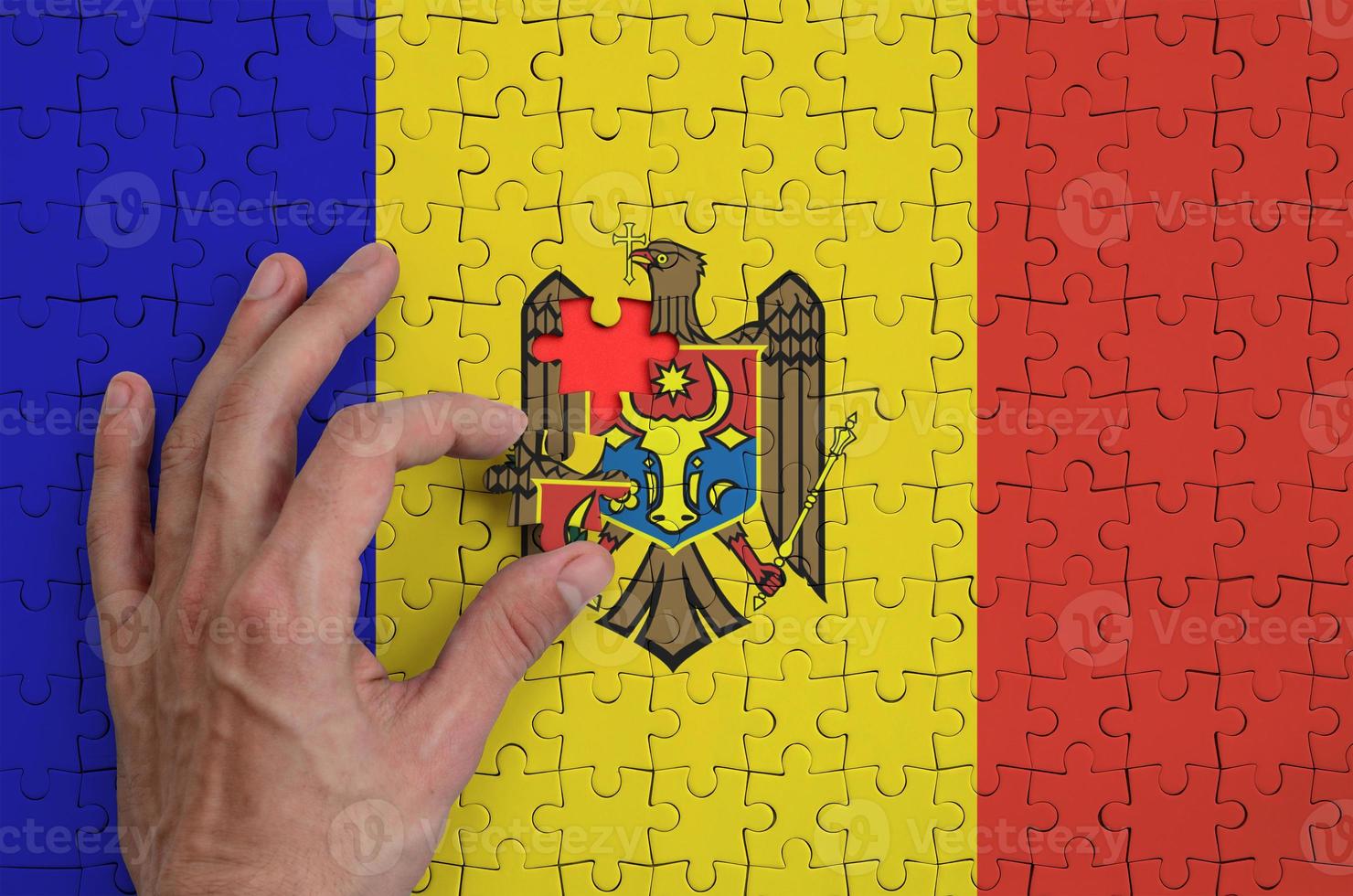 Moldova flag  is depicted on a puzzle, which the man's hand completes to fold photo