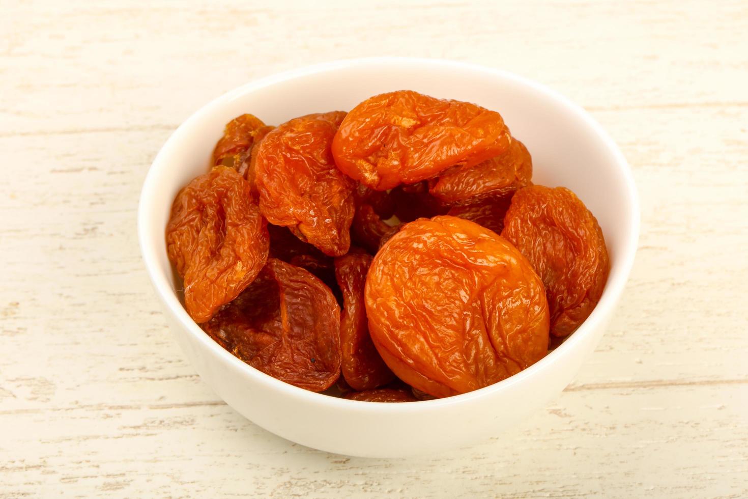 Dried apricots in a bowl on wooden background photo