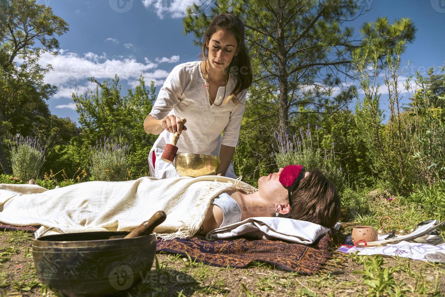 Woman therapist practicing sound healing therapy on a woman lying. photo