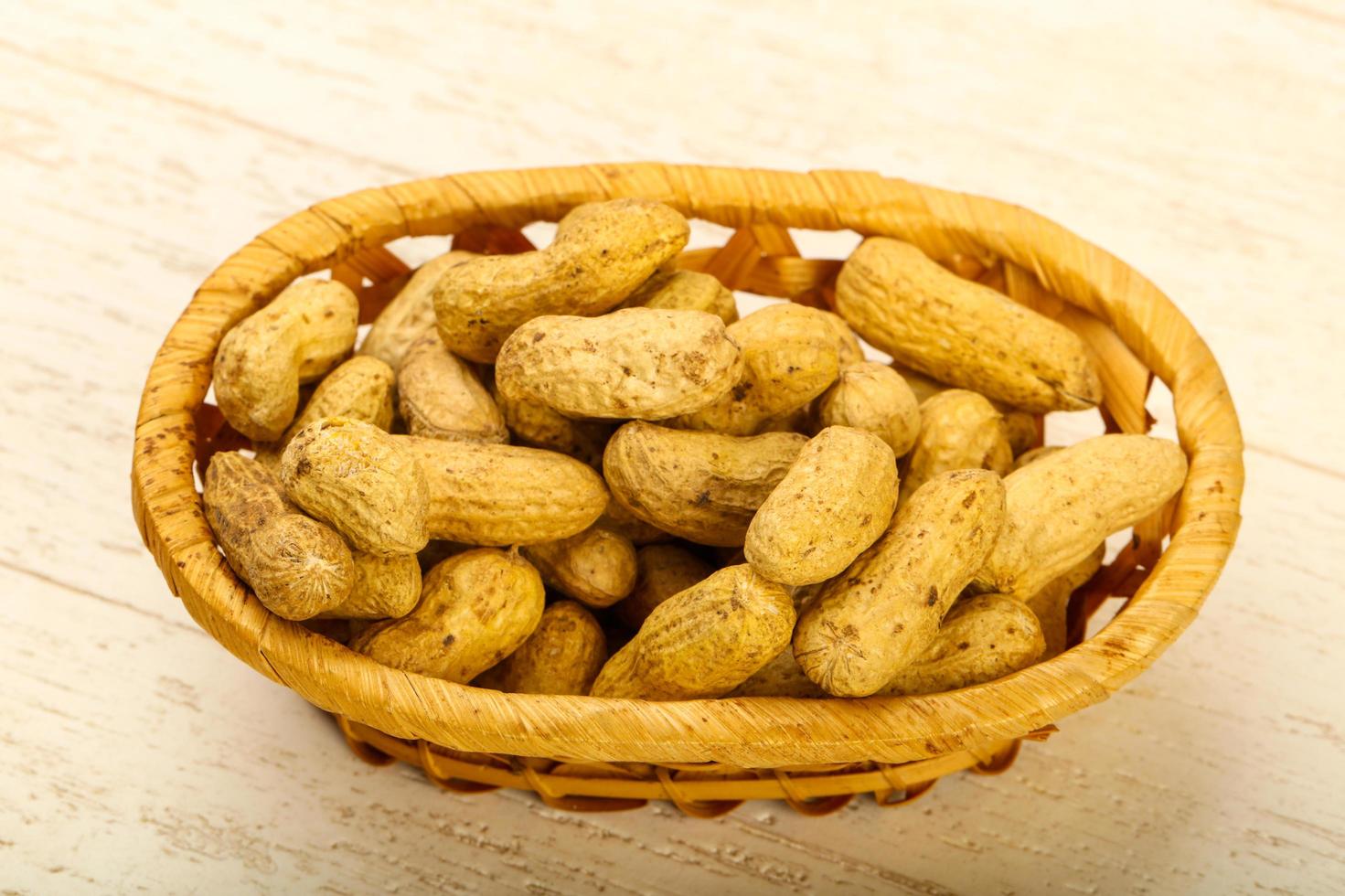 Unpeeled peanuts in a basket on wooden background photo