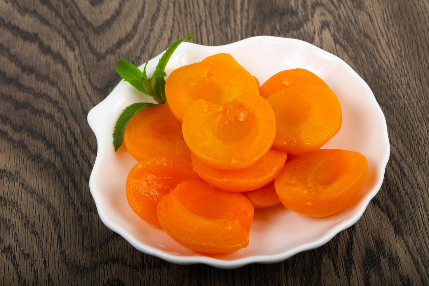 Canned apricots in a bowl on wooden background photo