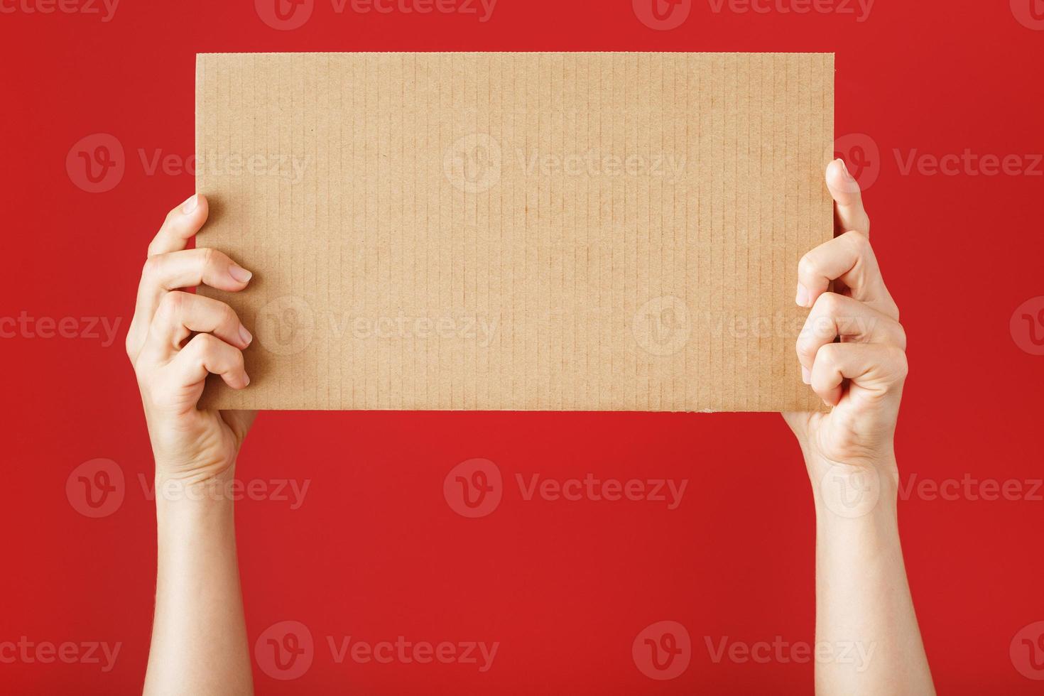 Hands holding a blank sheet of cardboard on a red background. photo