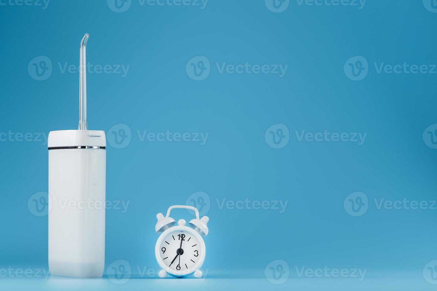 Irrigator oral cleaning with alarm clock on blue background. photo