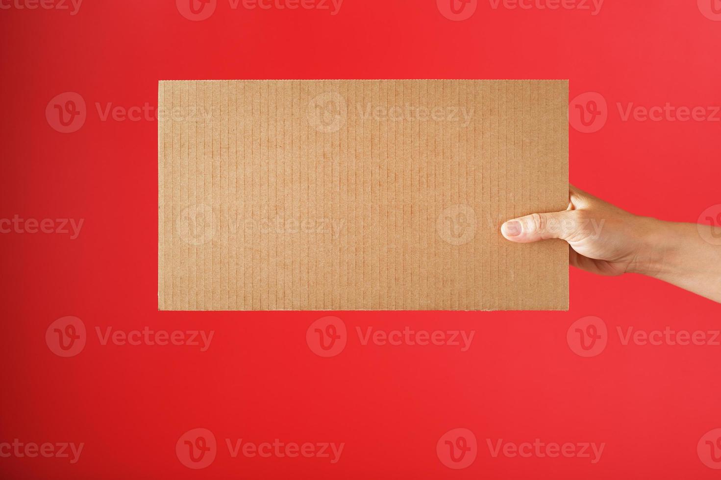 Hand holding a blank sheet of cardboard on a red background. photo