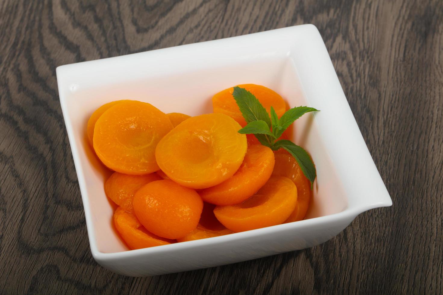 Canned apricots in a bowl on wooden background photo