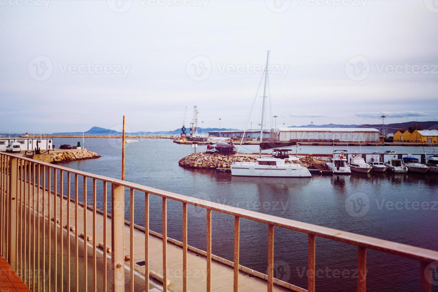 foto de la zona peatonal del rompeolas del puerto con yates y barcos amarrados al fondo