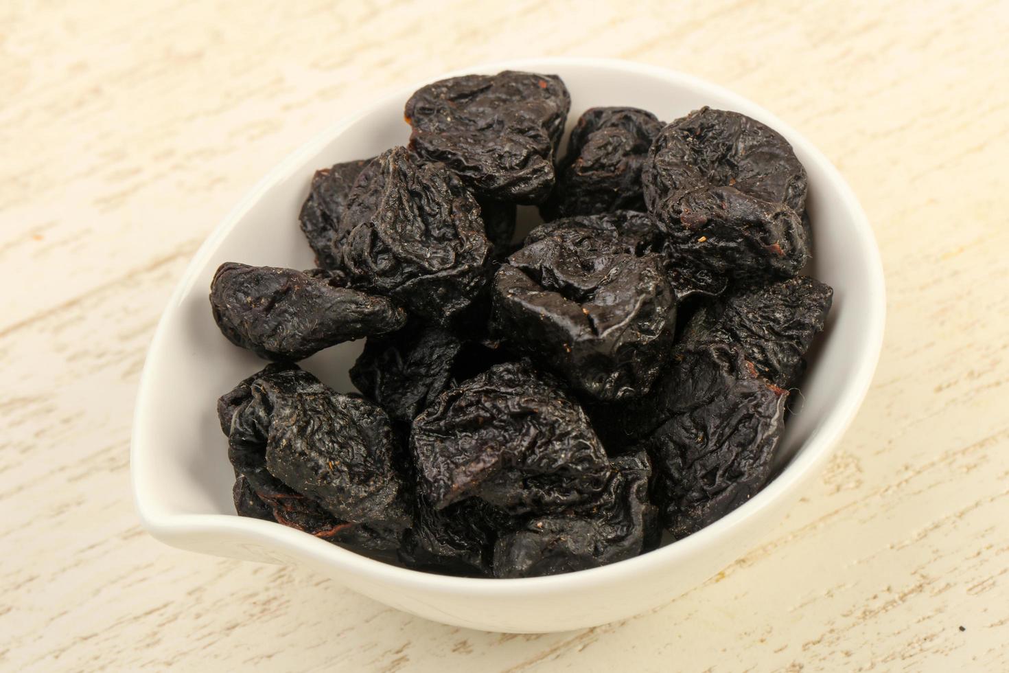 Dried plums in a bowl on wooden background photo