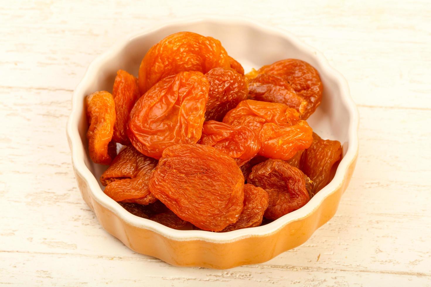 Dried apricots in a bowl on wooden background photo