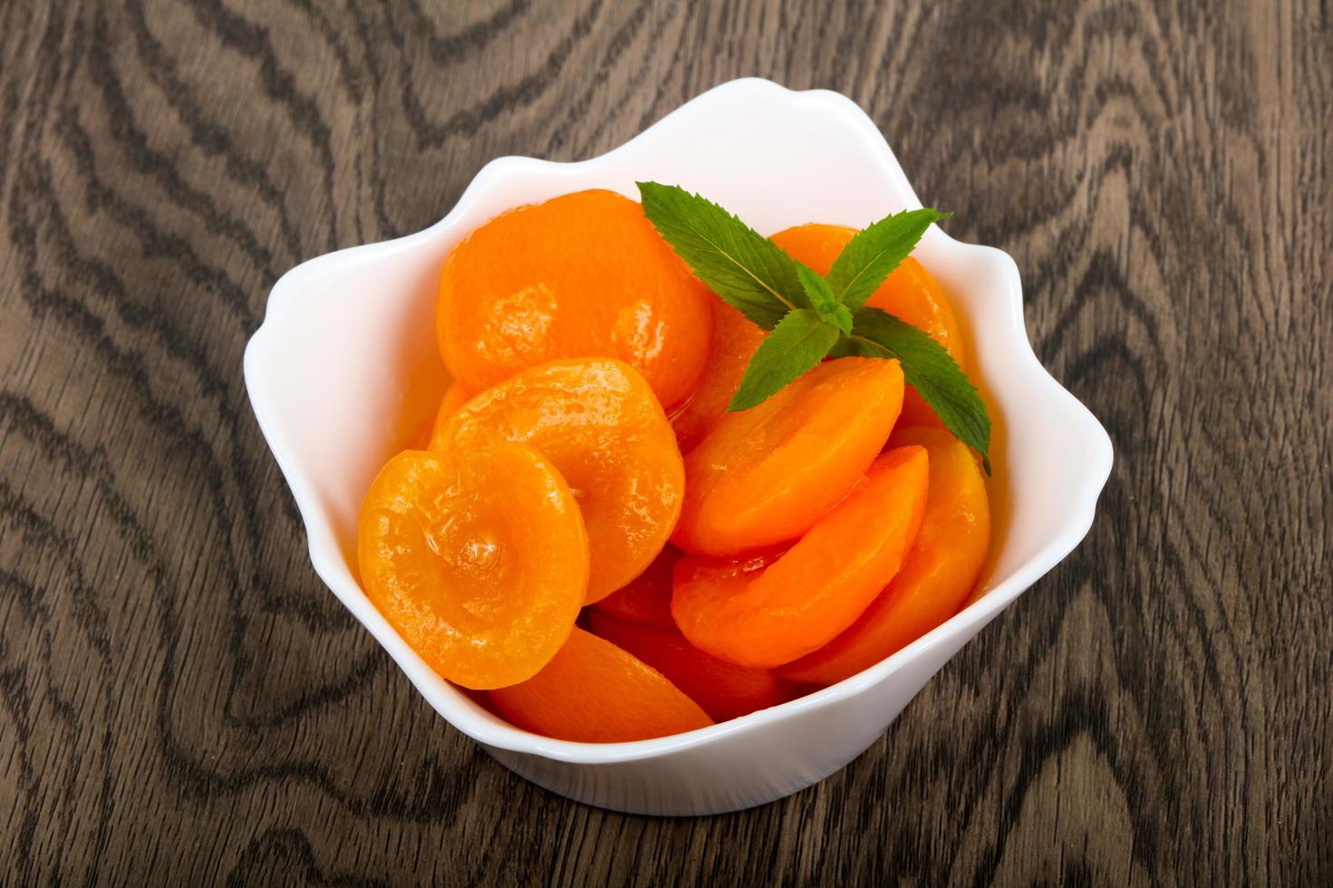 Canned apricots in a bowl on wooden background photo