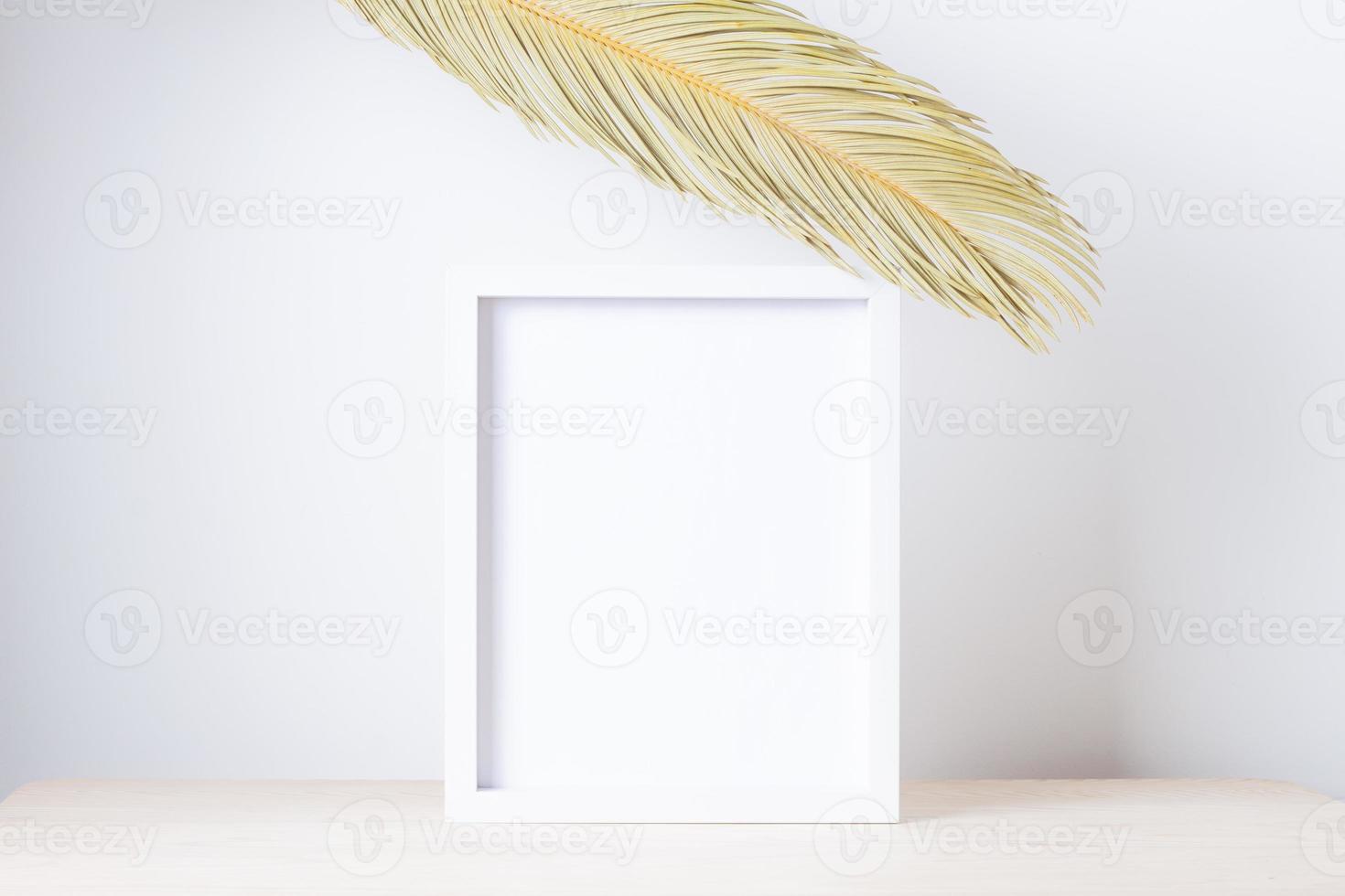 Home decoration with white mock up frame and palm leaf on table. Artwork showcase. Close up, copy space photo