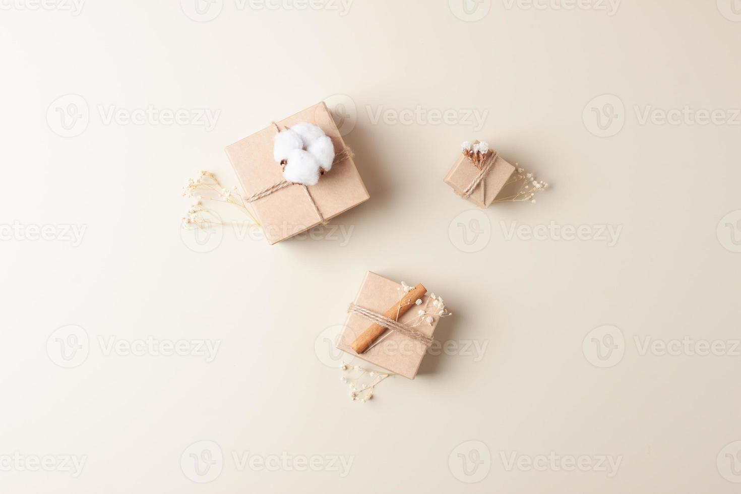 Christmas minimal composition with packaging gifts in craft paper and flowers on beige background. Zero waste Christmas holiday concept. Flat lay, copy space photo