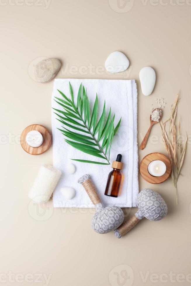 tratamiento de spa con botella cosmética, velas y bolsa de hierbas, toalla sobre fondo beige. endecha plana foto