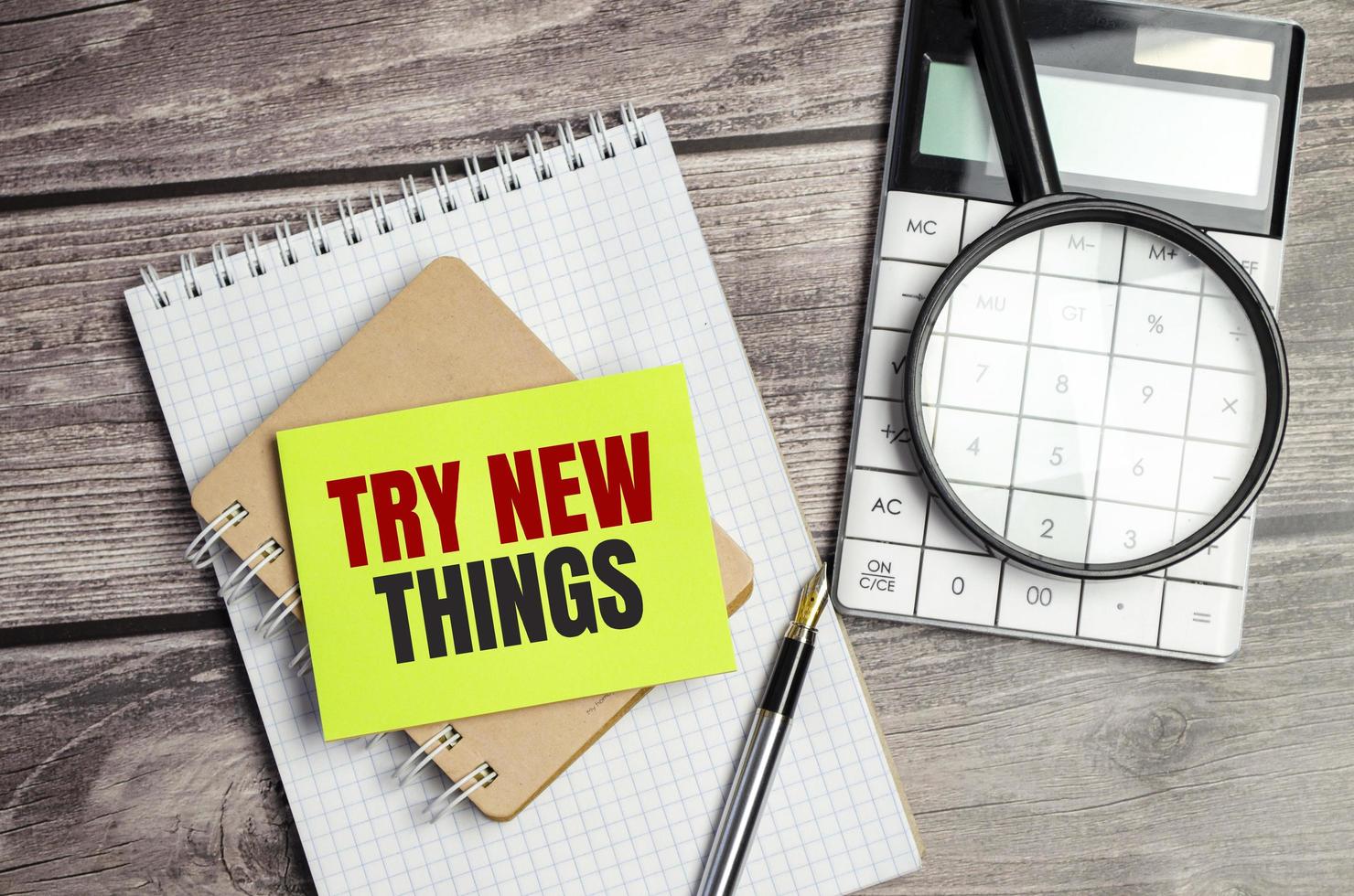 TRY NEW THINGS words on green sticker and calculator, magnifying glass on wooden background photo