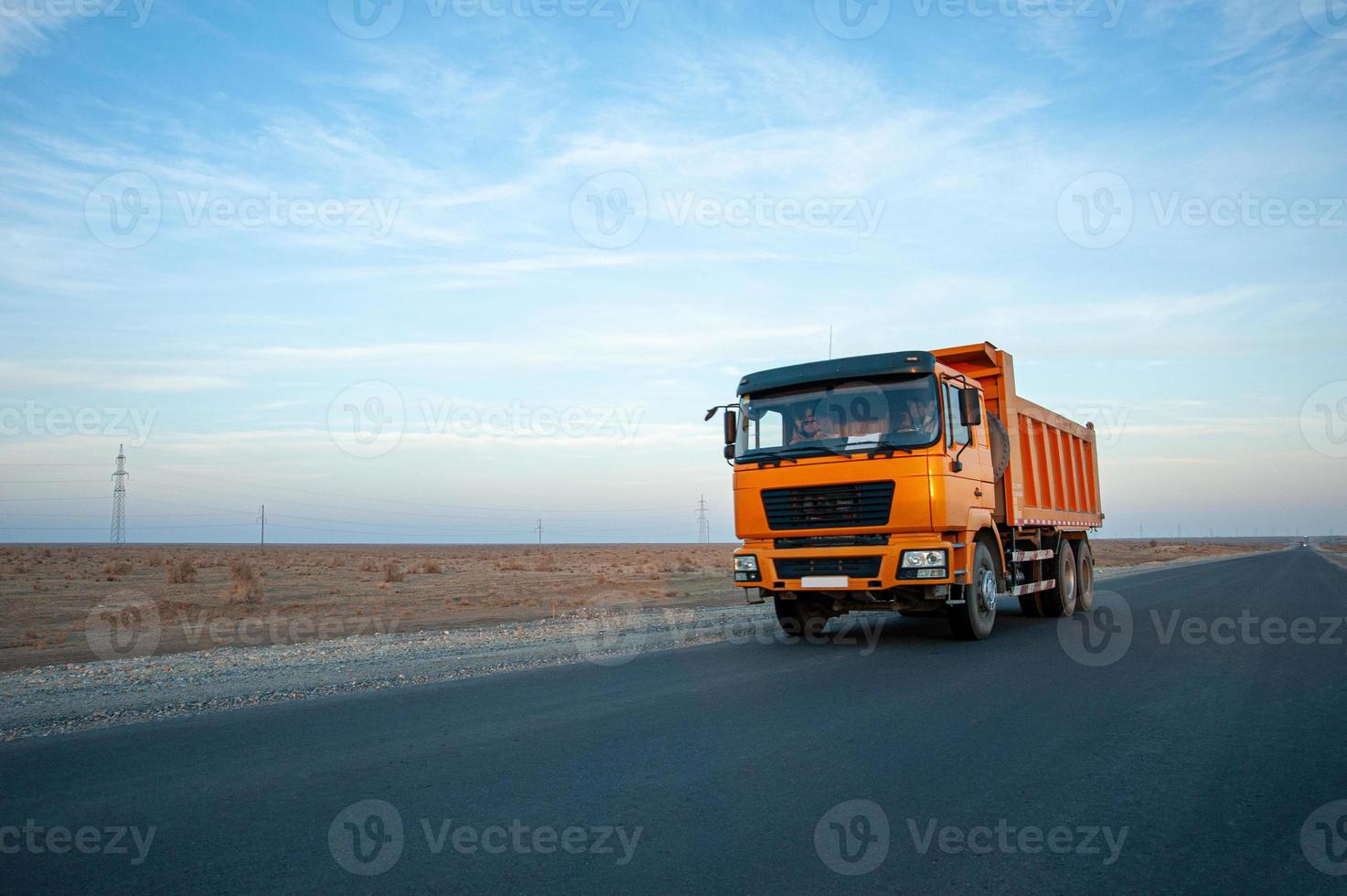 An orange dump truck on a desert road against a beautiful sky background photo