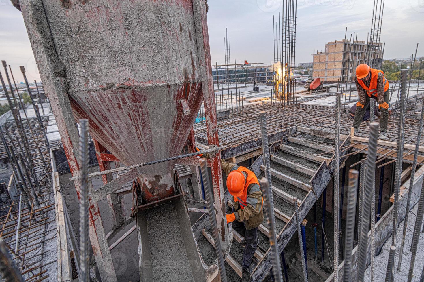 The workers on a building infrastructure roof with machinery and tools. Pouring concrete into a mold photo