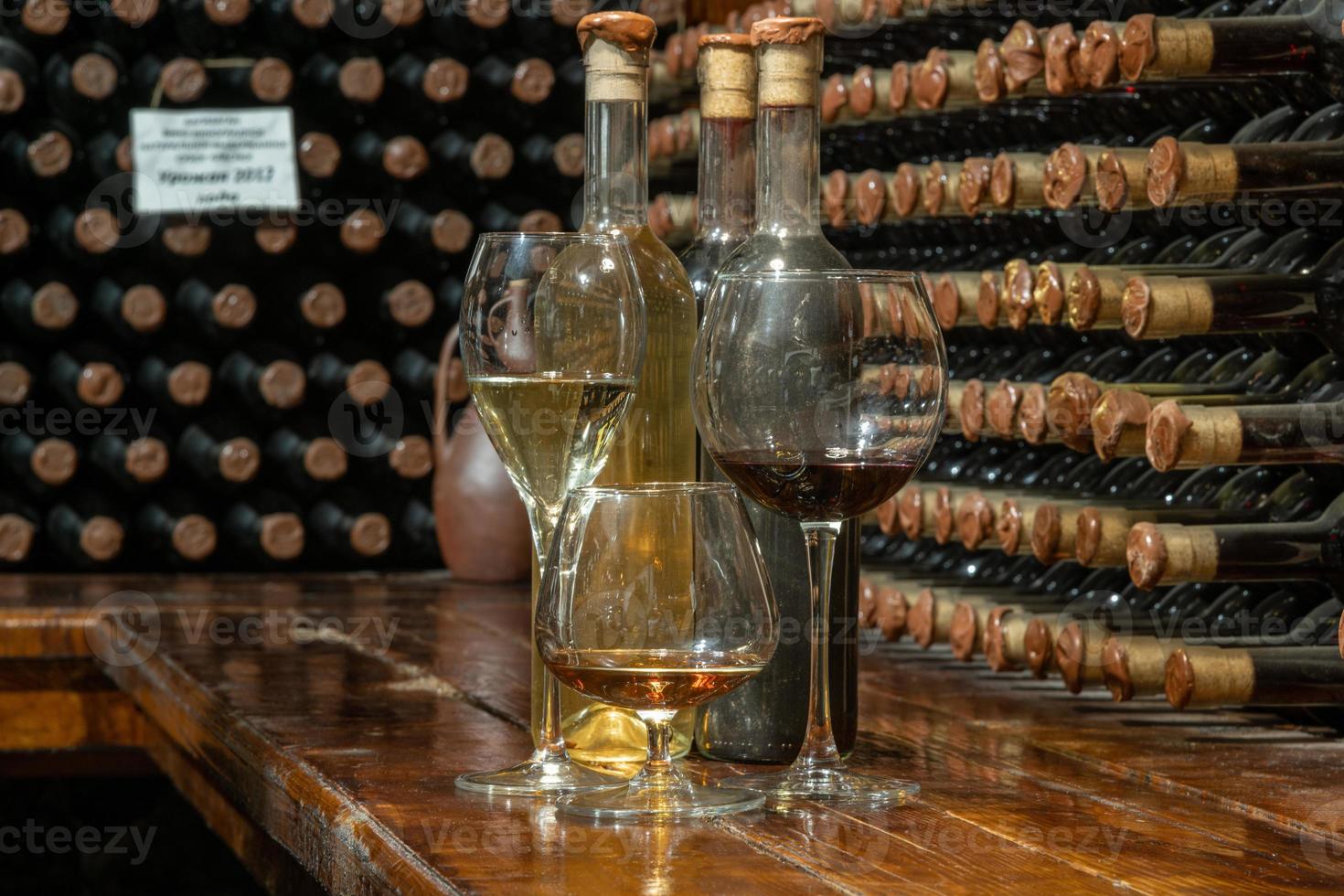 A closeup of bottles of different types of wine with a wine cellar in the background. Wine tasting photo