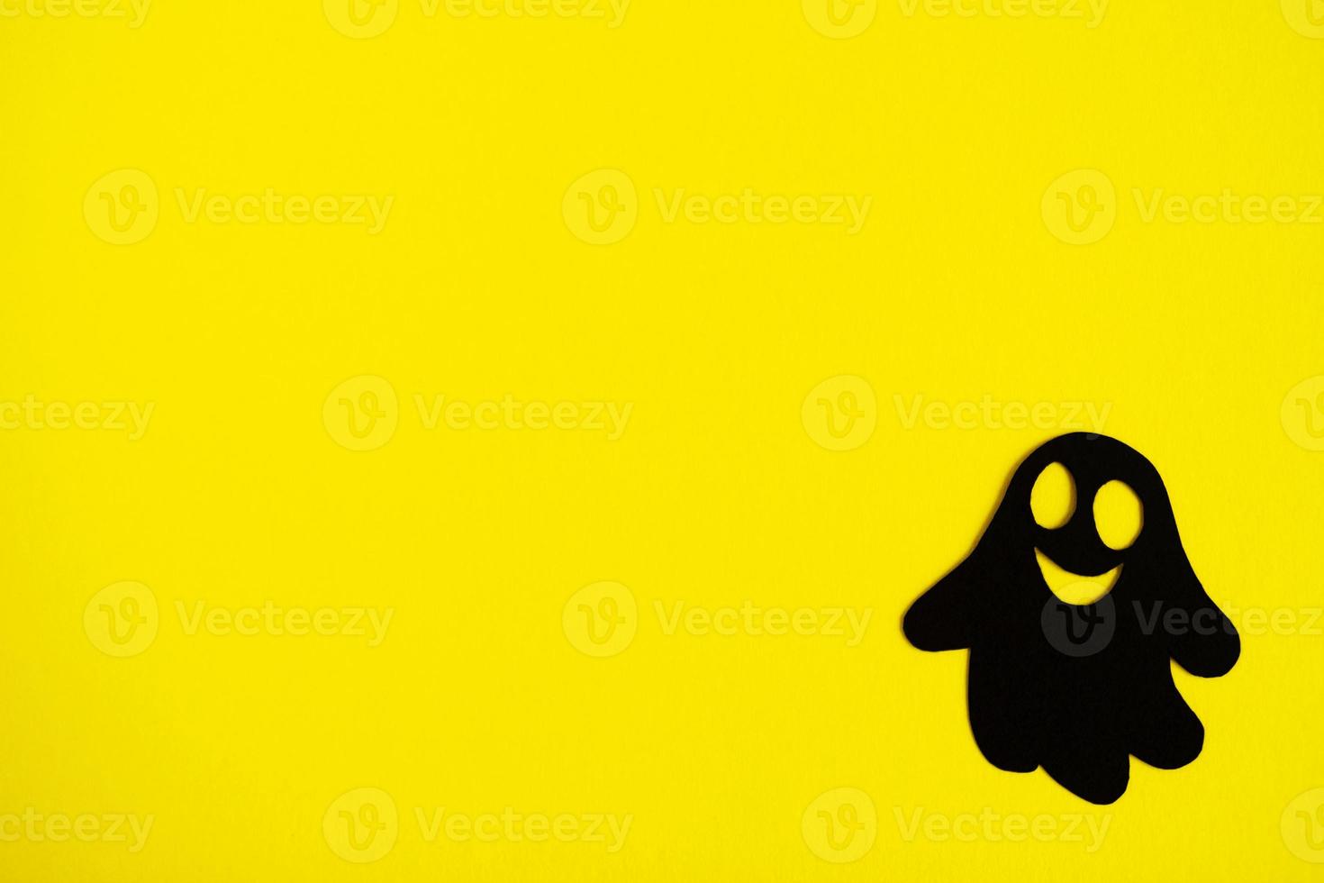 Holiday decorations for Halloween. Black paper ghost on a yellow background, top view. photo