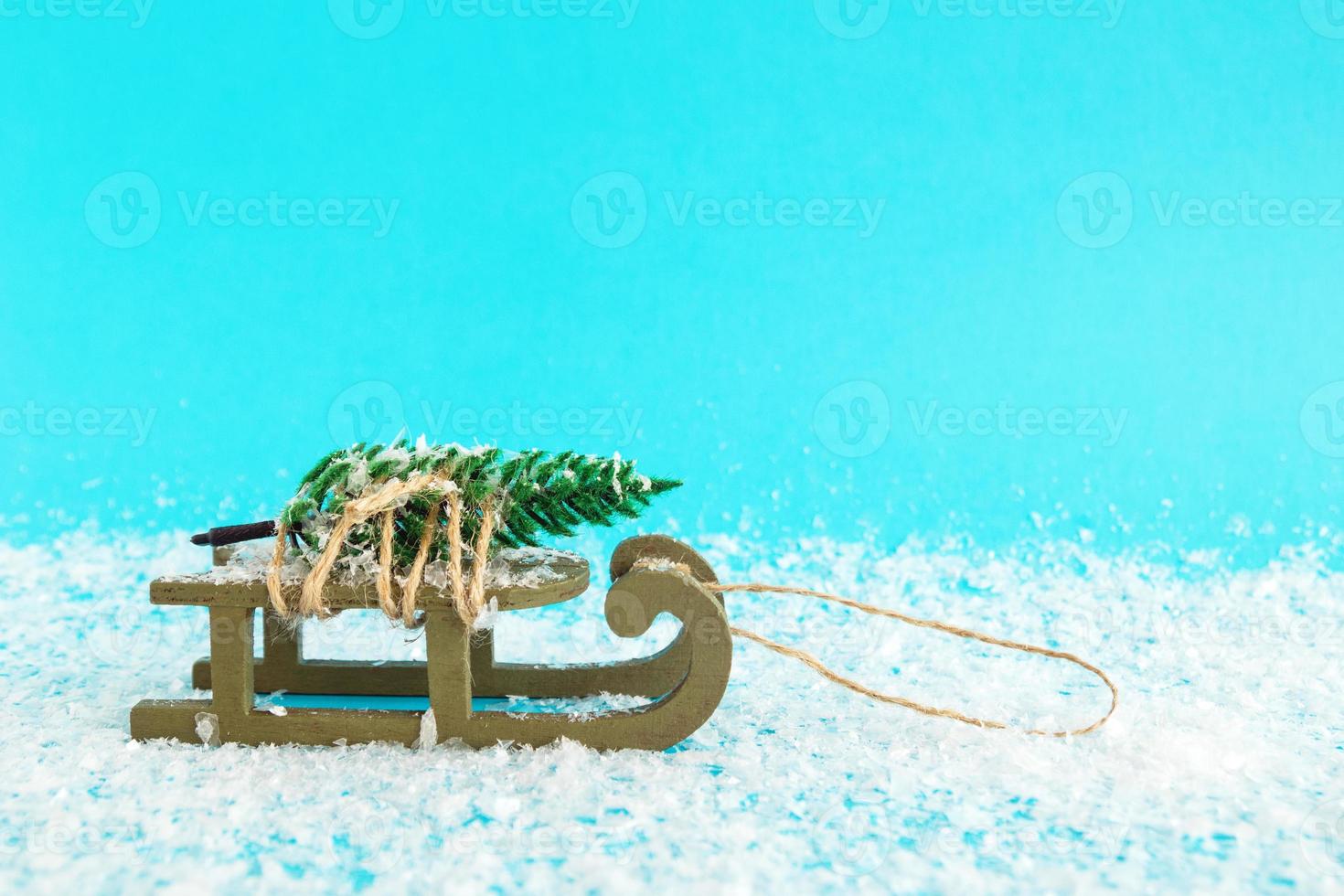 Green wooden sleigh with tied artificial fir tree on a blue background with artificial snow. Christmas and New Year concept with copy space. photo