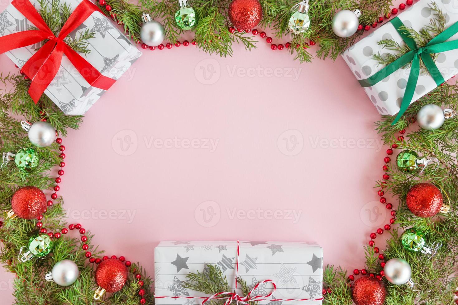 vista superior en un marco de adornos navideños rojos, verdes y plateados, cajas de regalo y ramas de abeto sobre un fondo rosa con espacio para copiar. foto